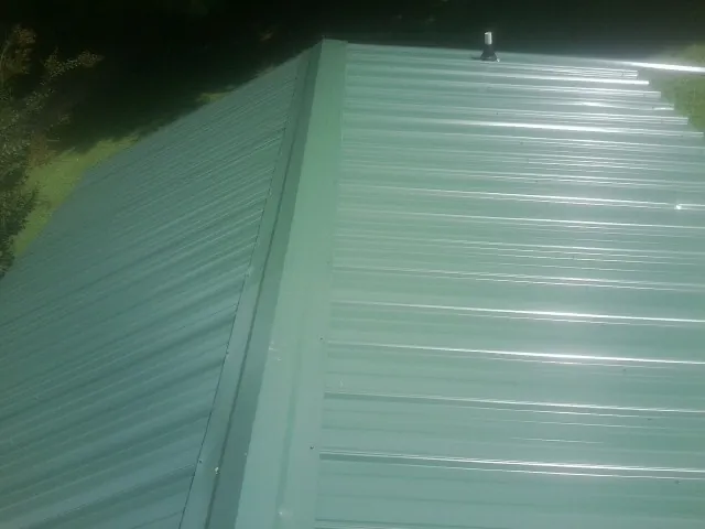 New green metal panels meeting at the ridge of a roof — Flat Roof Repair work by our crew in La Fayette
